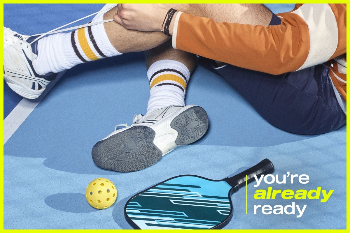 A man sat down tying his laces with a pickleball and padel next to him. There's a tagline that says 'you're already ready' in the bottom right.