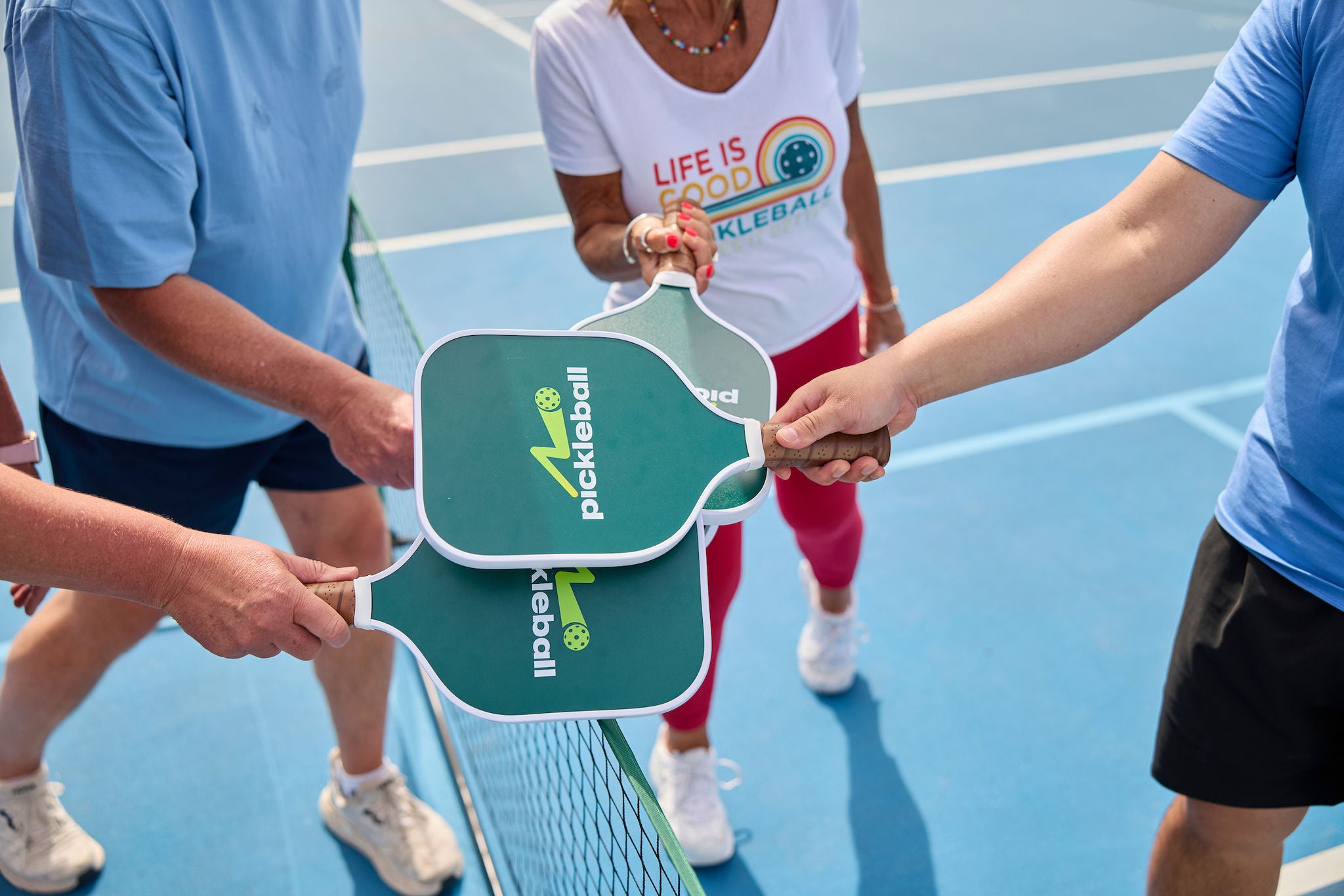 Four pickleball players tap paddles together prior to a game in a gesture of sportsmanship.