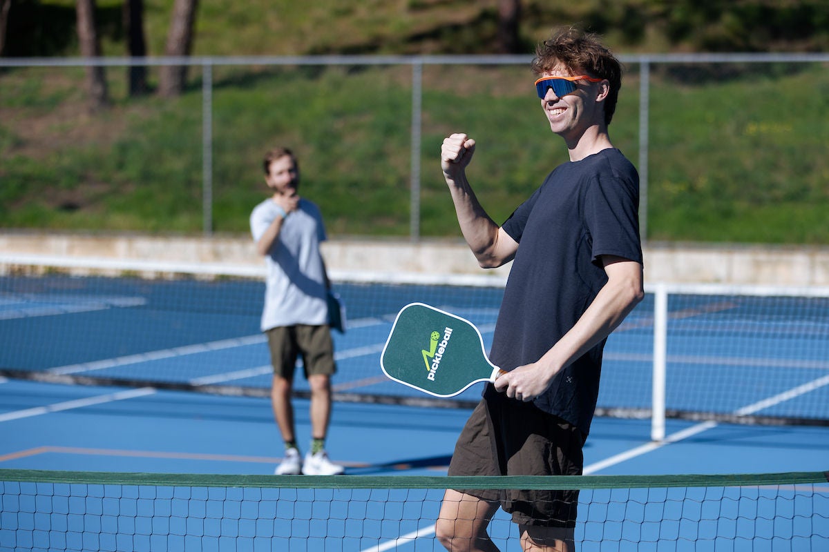 A male player holding a pickleball paddle celebrates on court