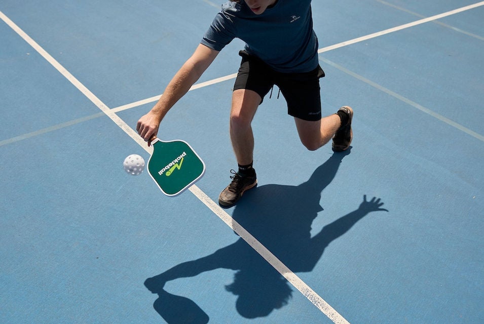 Close up of a pickleball player reaching to strike the ball with padel on court