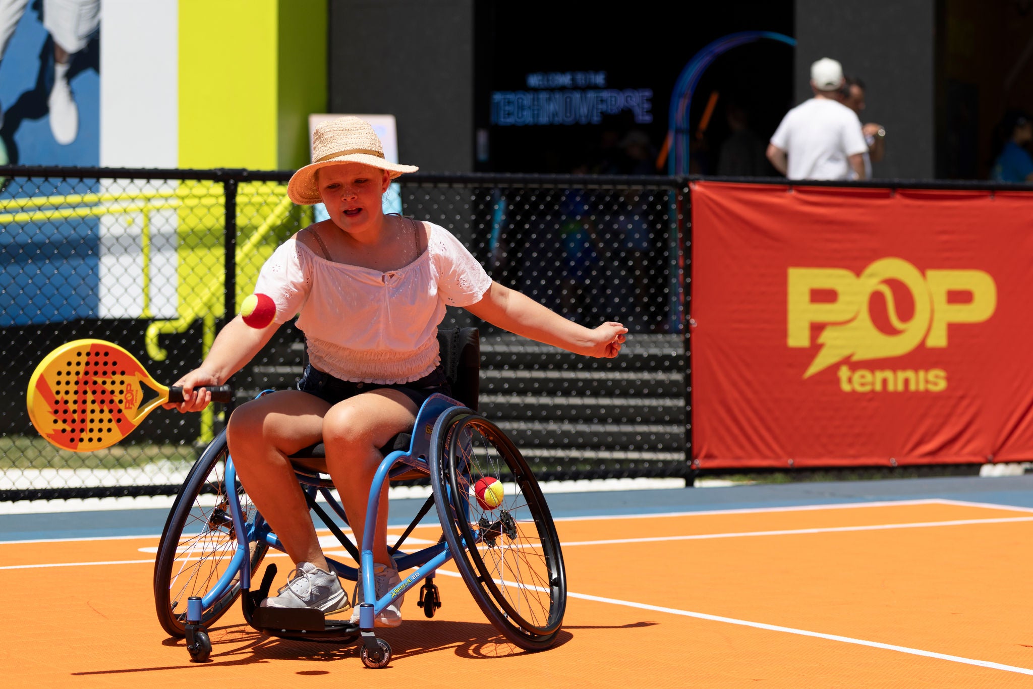 A player in a wheelchair enjoying playing POP Tennis on a bright orange court.