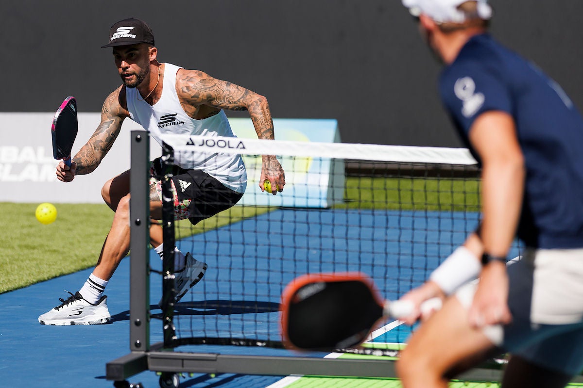 Two men playing pickleball. One out of focus in the foreround the other fully focussed on returning the ball.